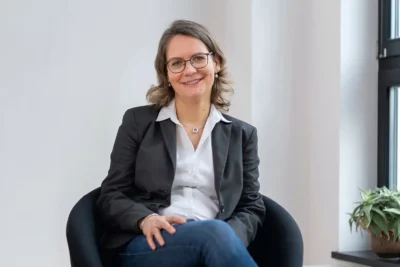 Businessportrait einer Managerin in Hemd und Sakko im Sessel sitzend vor cleaner Kulisse, fotografiert von Stefan Schubert.