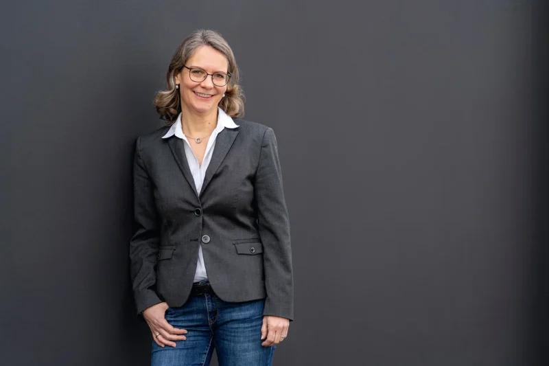 Businessportrait einer Unternehmerin in grauem Sakko, stehend vor minimalistischem Hintergrund in Berlin, Stefan Schubert Fotografie.