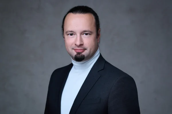 Mitarbeiterfoto im modernen Look: klassisches Outfit vor grau strukturiertem Hintergrund, fotografiert von Stefan Schubert.