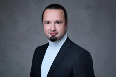 Mitarbeiterfoto im modernen Look: klassisches Outfit vor grau strukturiertem Hintergrund, fotografiert von Stefan Schubert.