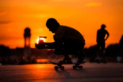 Videograf auf Skateboard am Filmset; Gegenlicht-Aufnahme in orangefarbener Abendsonne, fotografiert von Stefan Schubert.