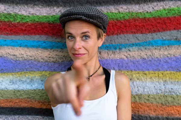 Direkter Blickkontakt: Künstlerin mit Schiebermütze vor bunt gestreifter Wand; Sedcard-Fotografie Stefan Schubert.