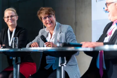 Lächelnde Teilnehmer bei einer Symposium-Diskussion einer Fachmesse in Berlin; Veranstaltungsfotografie Stefan Schubert.