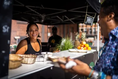 Event-Catering: Lachende Mitarbeiterin an einem Streetfood-Stand beim AFFB Berlin; Eventfotografie von Stefan Schubert