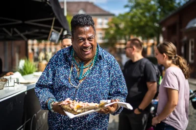 African-Foodfestival in Malzfabrik Berlin: Begeisterter Gast mit frisch zubereitetem Fisch am Foodstand; von Stefan Schubert