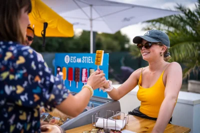 Sommer-Eventfotografie: Gast erhält Eis am Stiel an einem mobilen Stand – Authentisches Festival-Foto von Stefan Schubert